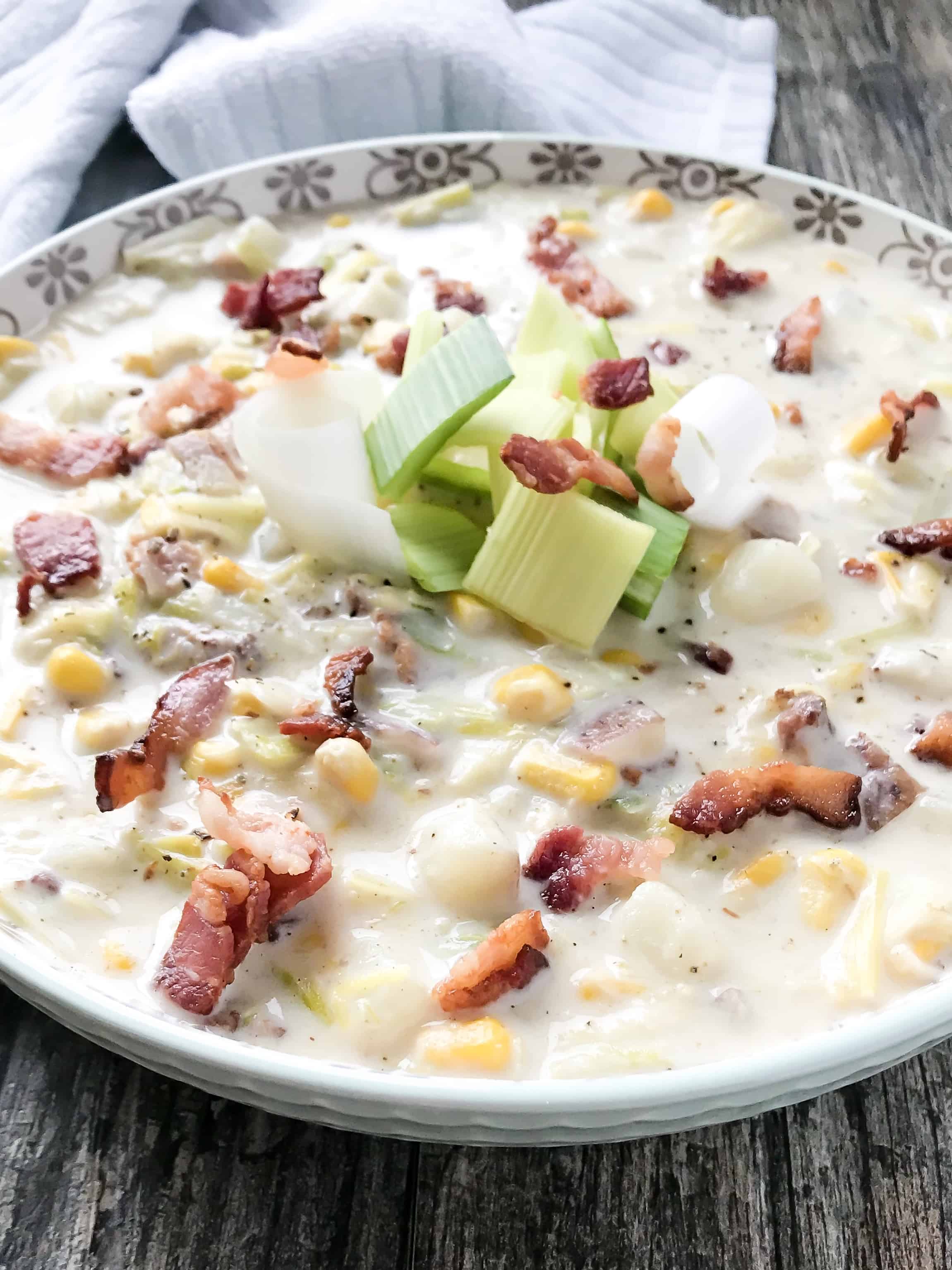 leek and corn chowder in a serving bowl, garnished with fresh leeks and bacon