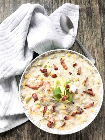 leek and corn chowder in a serving bowl, garnished with fresh leeks and bacon