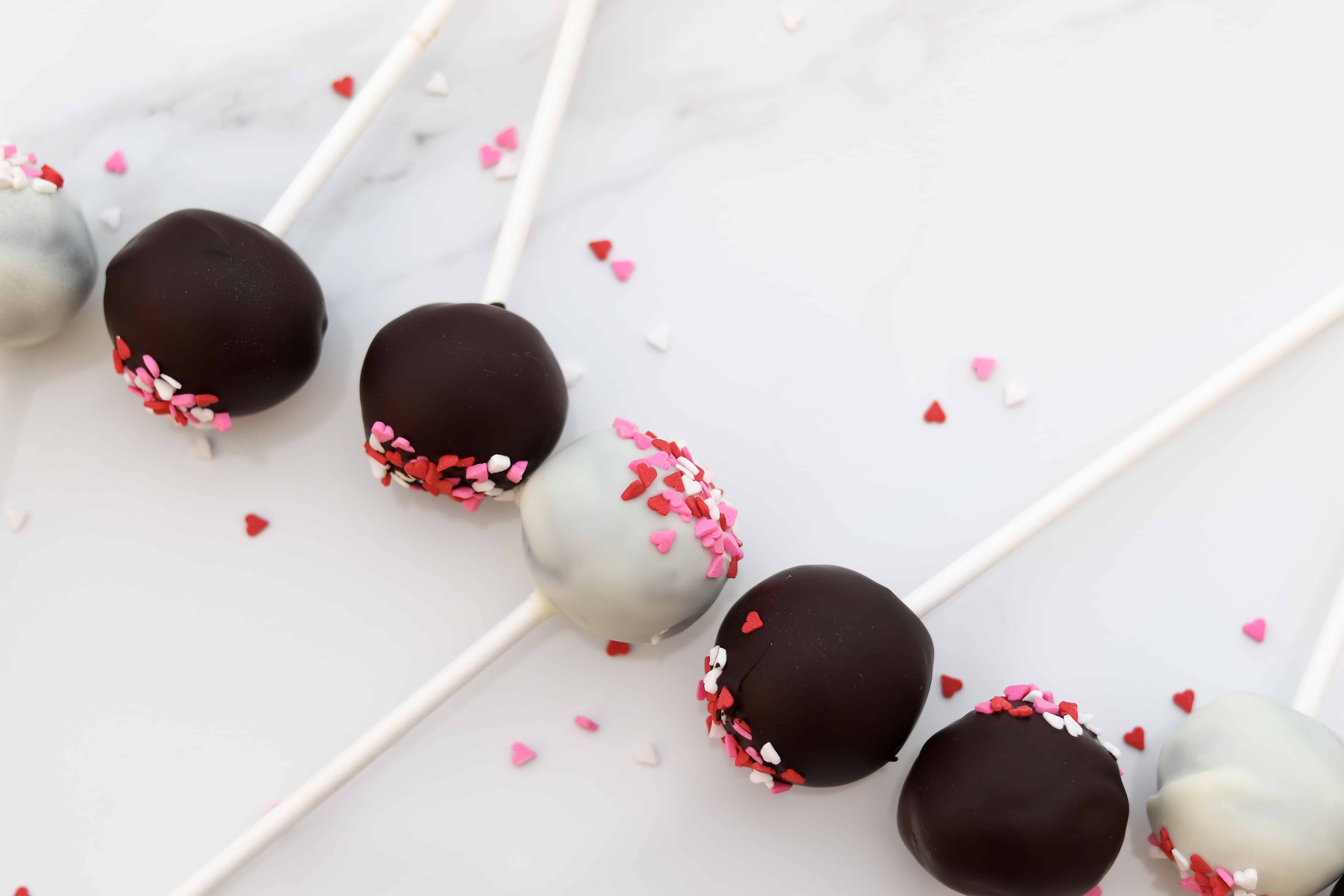 cake pops in vertical line with heart sprinkles surrounding them