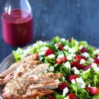 strawberry goat cheese chicken salad with berry vinaigrette on a grey plate, and a bottle of berry vinaigrette in the background