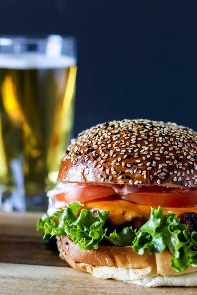 a blackened chicken sandwich on a wooden serving board with a beer in the background