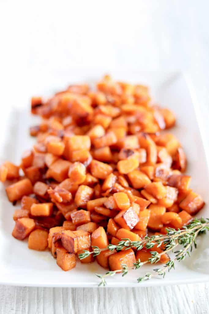 Pan Fried Maple Sweet Potatoes on a white serving plate with fresh sprigs of thyme in the corner