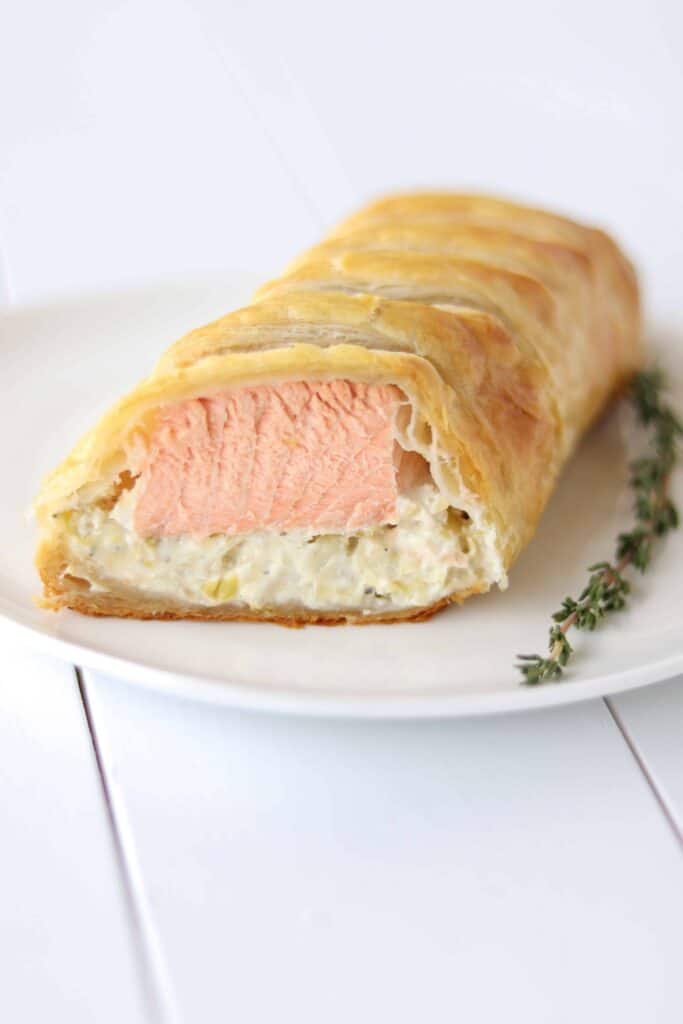 Close up of a piece of salmon wellington sliced open showing the cooked salmon and artichoke layers