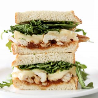 Aprict brie chicken sandwich stacked with arugula sprinkled around the background