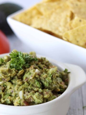 bowl of guacamole with tortilla chips in the background