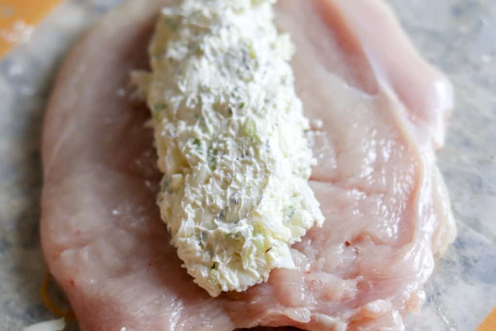 a raw chicken breast butterflied open and being stuffed with cream cheese
