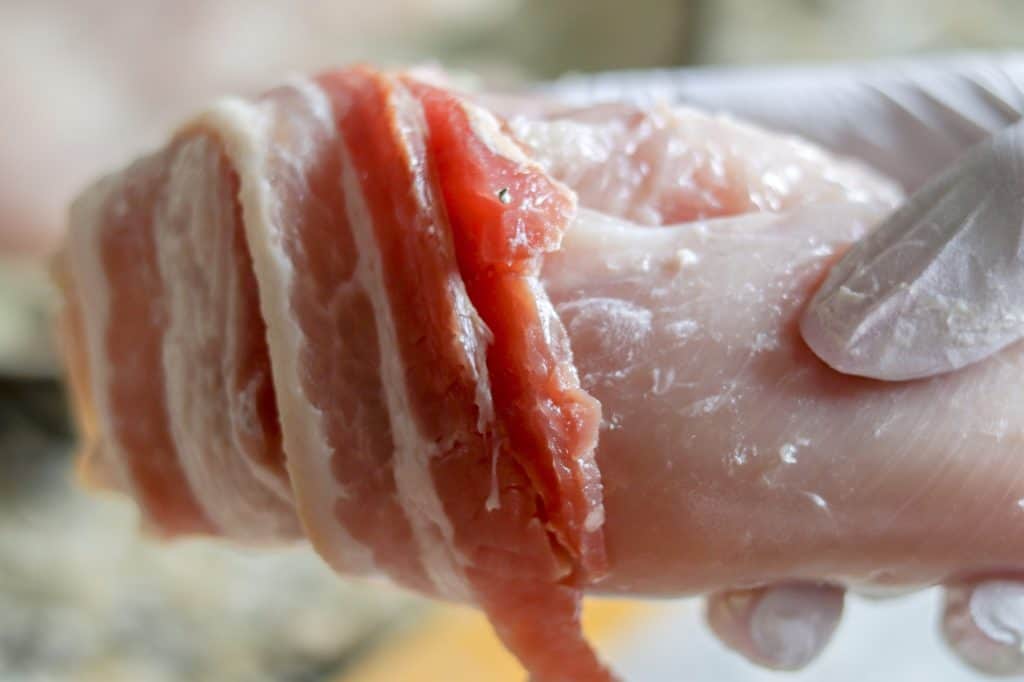 chicken breasts stuffed with cream cheese being wrapped in bacon