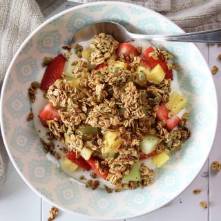 a bowl of yogurt, fruit, and topped with maple walnut and honey granola with a spoon on the edge