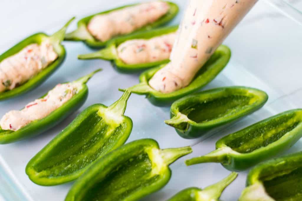 using a piping pag to fill the jalapeno poppers