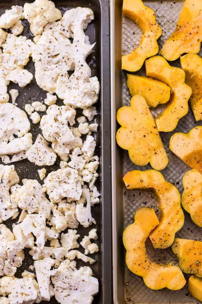 cauliflower and acorn squash on a sheet pan ready to be roasted in the oven