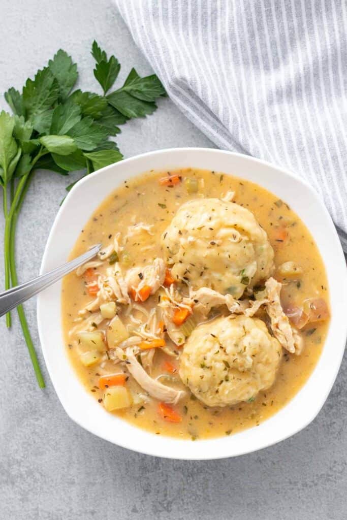 a bowl of chicken and dumplings with a sprig of fresh parsley on the side