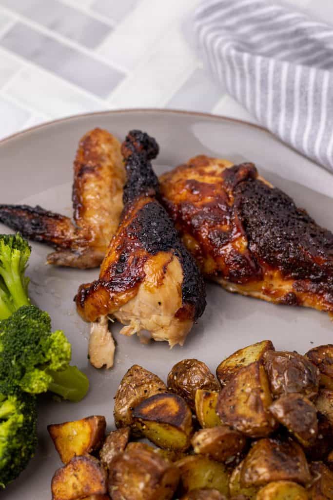 Bourbon Barbecue Roast Chicken pieces cut and served on a grey plate with pan fried hash browns and steamed broccoli