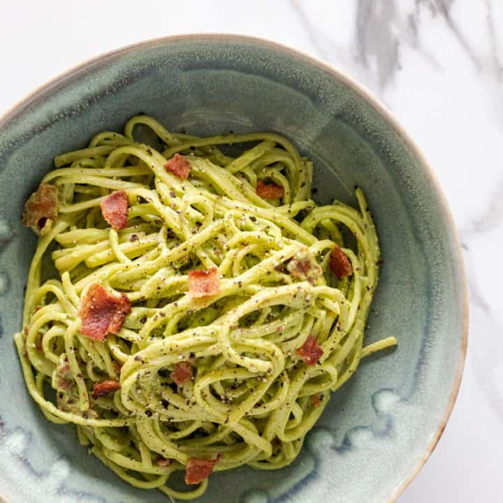 avocado carbonara served in a blue bowl topped with a little bit of extra bacon