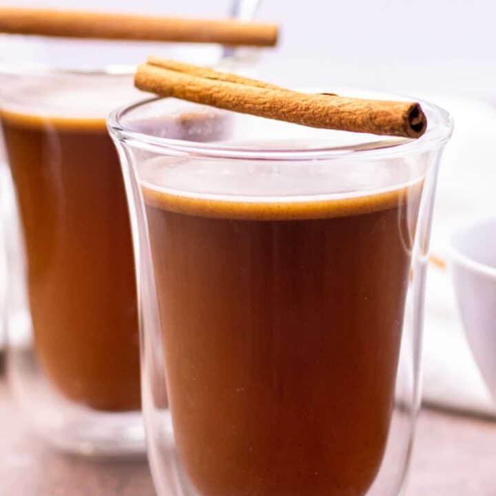 two prepared hot buttered rums in glass coffee mugs, each served with a cinnamon stick on top