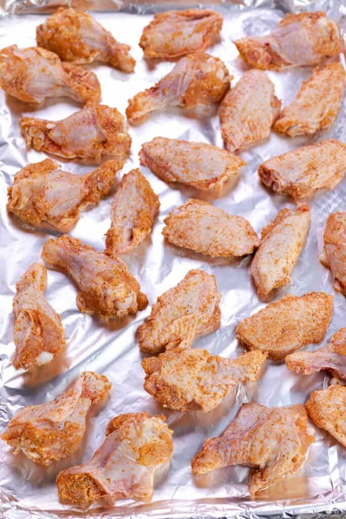 spreading out the raw chicken wings on a baking sheet lined with aluminum foil