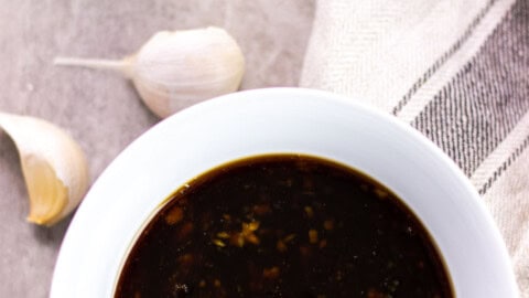 honey garlic sauce in a white serving bowl with cloves of fresh garlic in the background