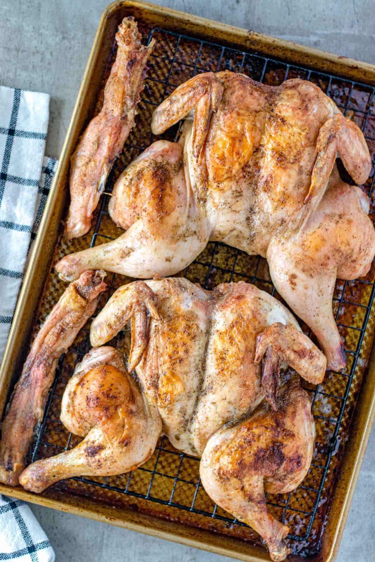 Two fully cooked spatchcocked chickens on a baking sheet.