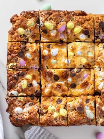 a prepared batch of mini egg cookie bars cut into 16 pieces on a marble background