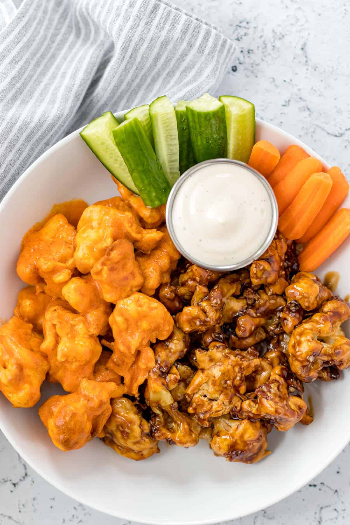 buffalo cauliflower wings and teriyaki cauliflower wings in a bowl served with a side of veggies and ranch dressing for dipping