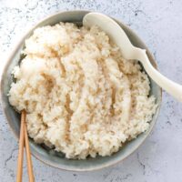 sushi rice in a blue bowl with a pair of chopsticks and a rice server