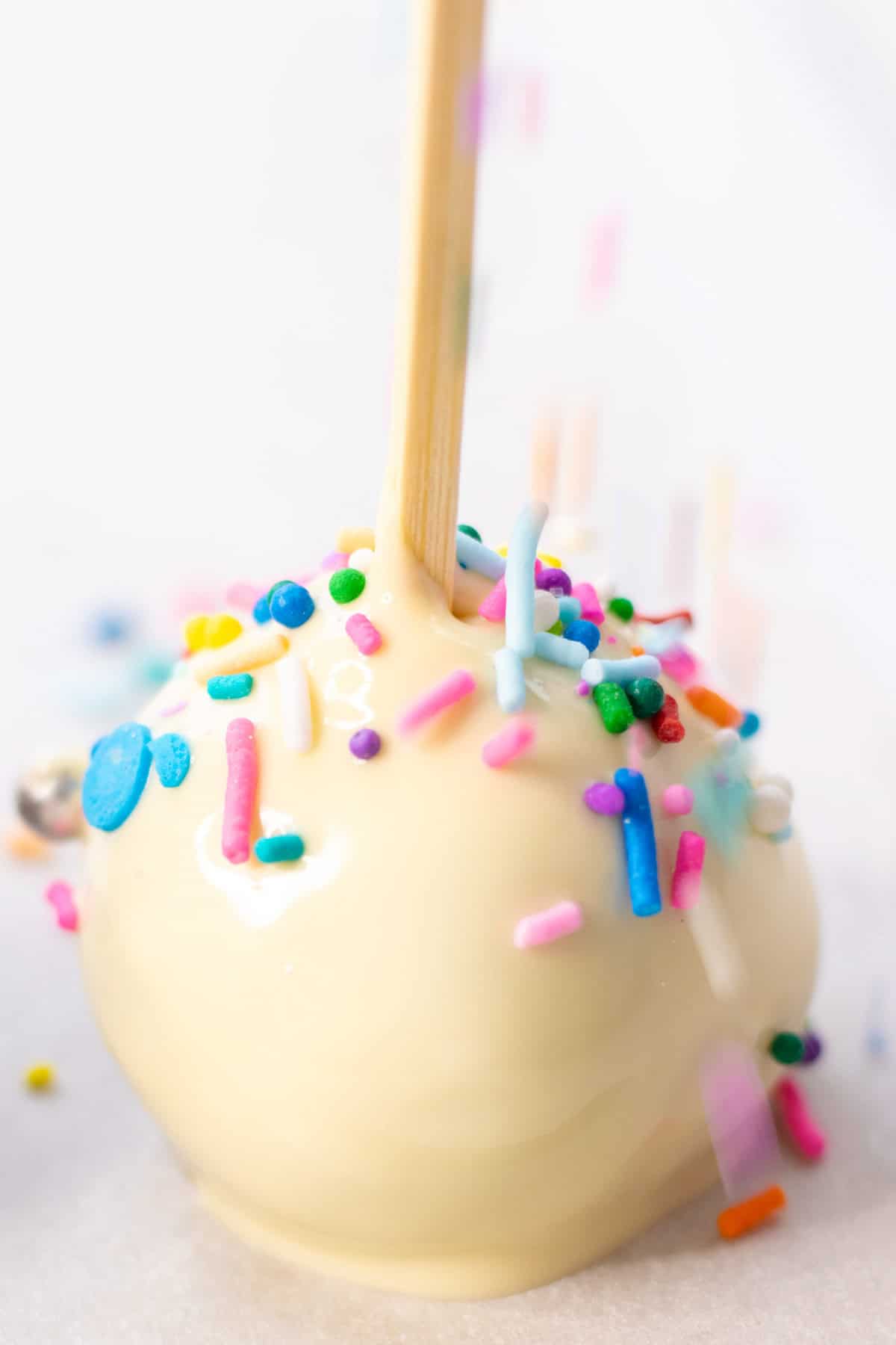 Sprinkling colourful sprinkles on top of the freshly coated cake ball.