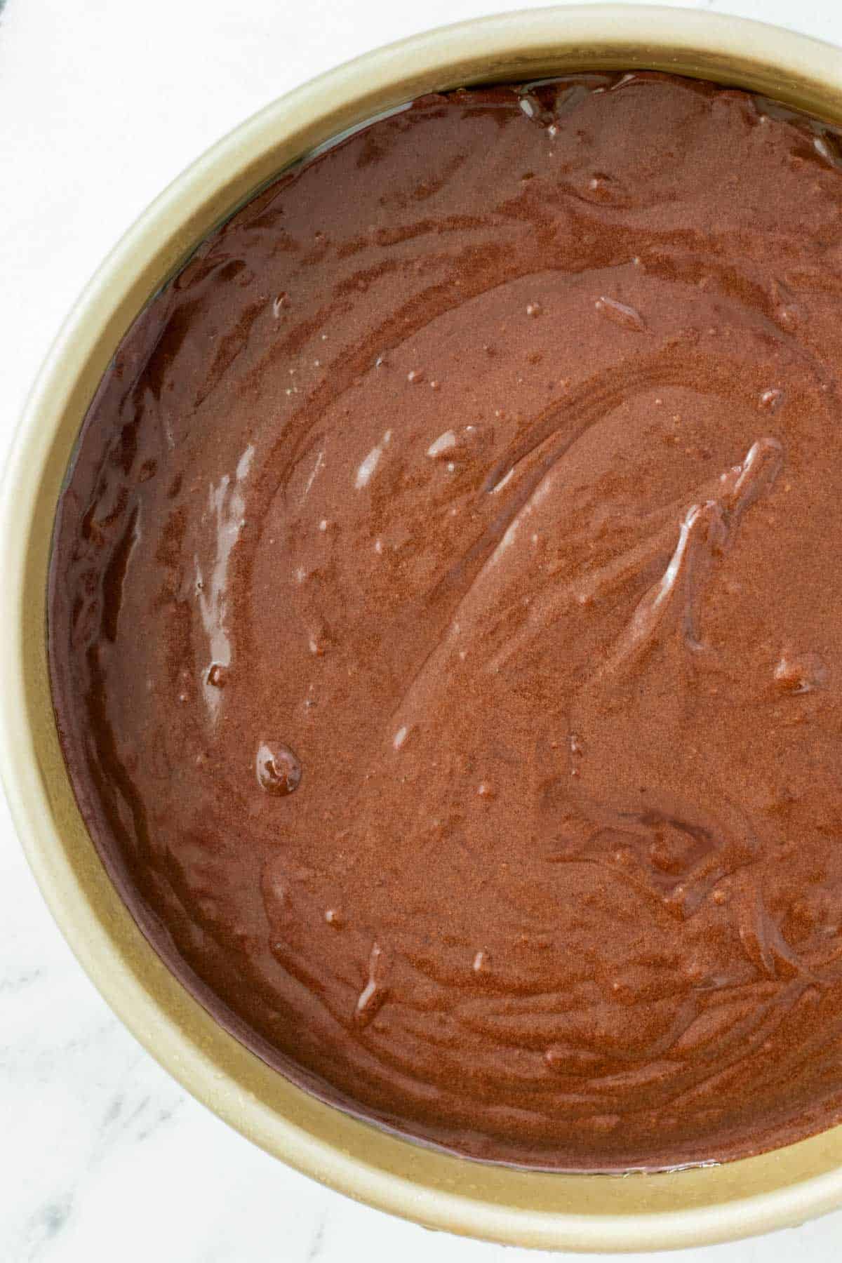 Chocolate cake batter poured into a greased cake pan.
