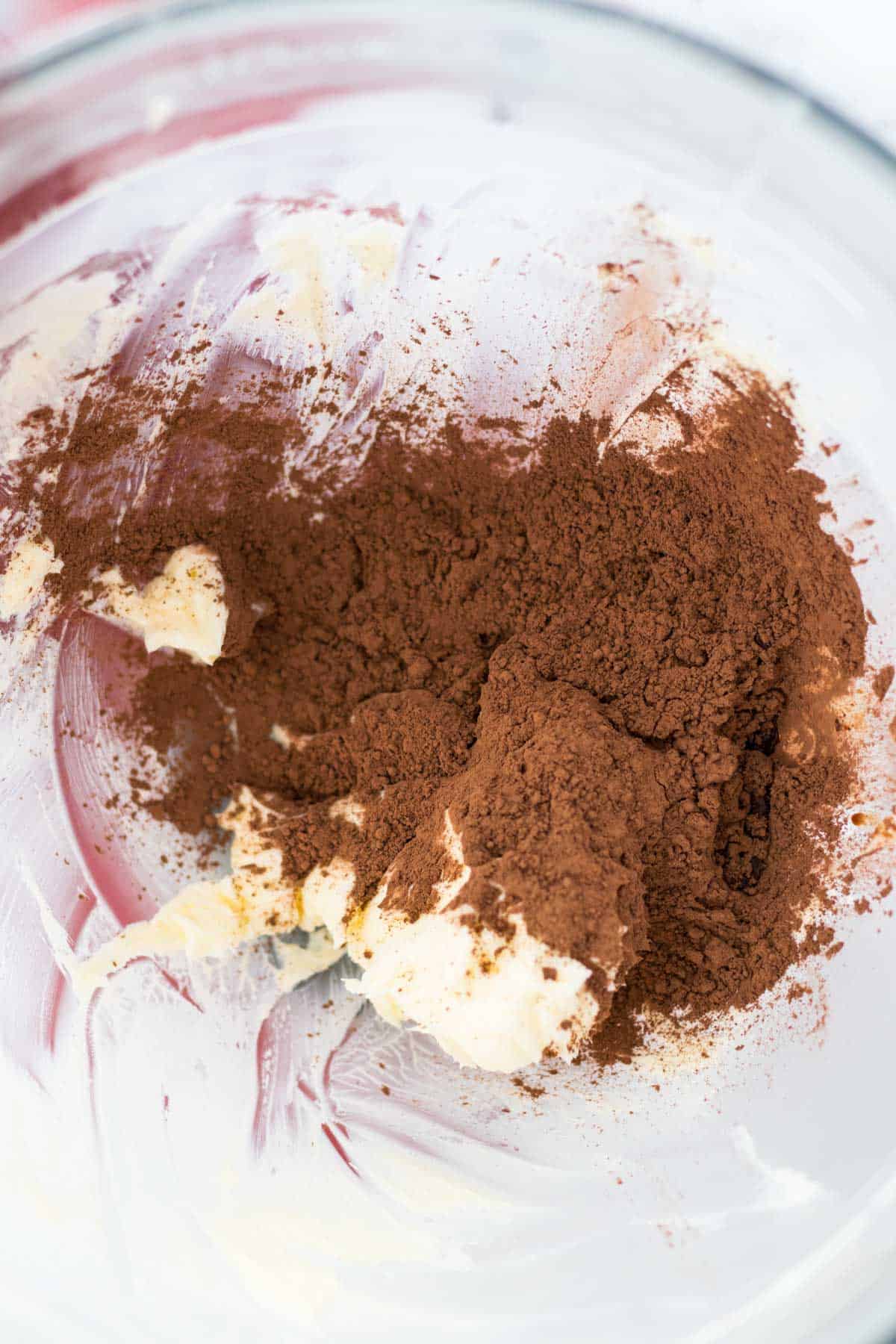 Adding the cocoa powder to the whipped butter in the mixing bowl.