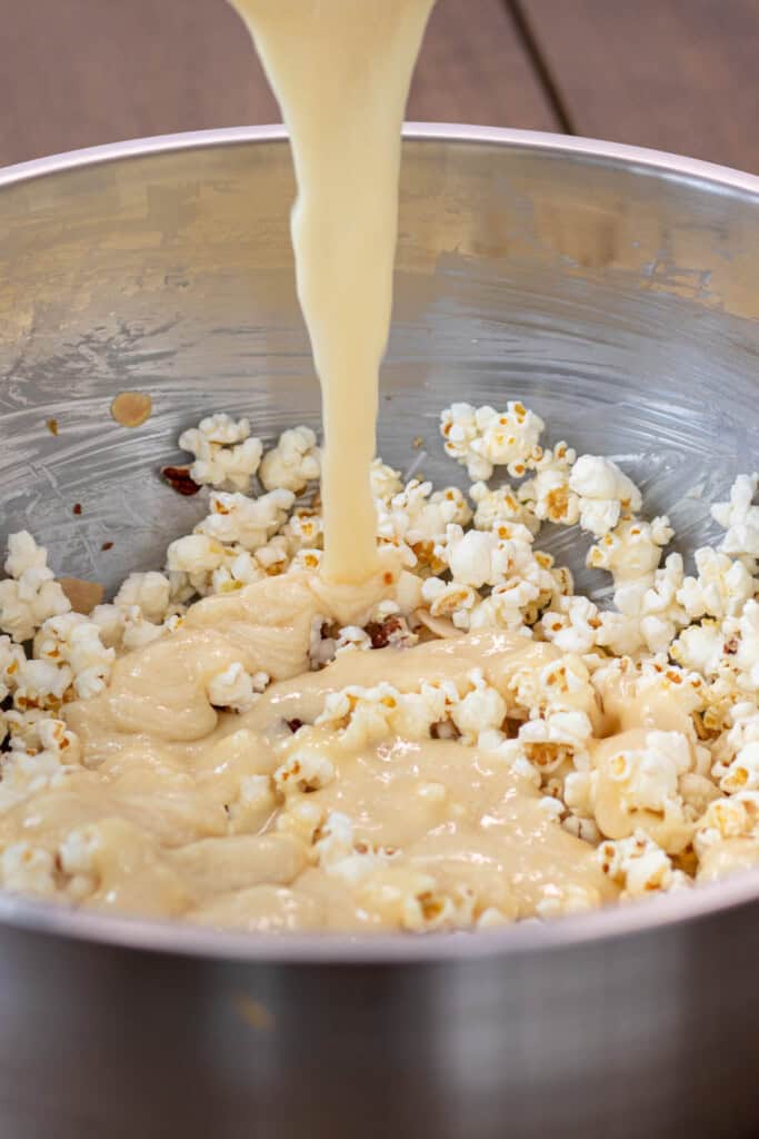 Pouring the caramel sauce onto the popcorn and nuts in a large mixing bowl.