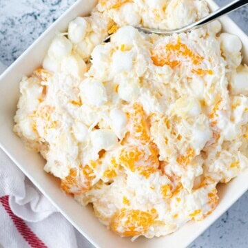 Light and fluffy ambrosia salad in a square white serving bowl with a silver spoon.