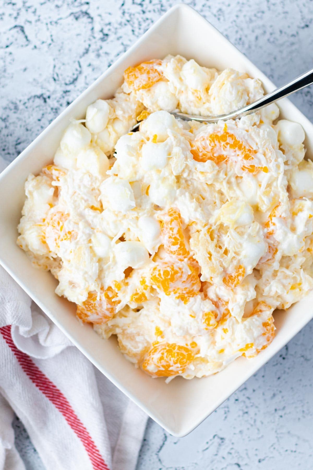 Light and fluffy ambrosia salad in a square white serving bowl with a silver spoon.
