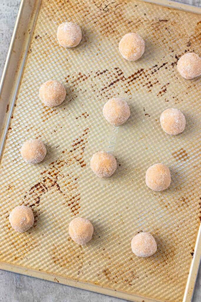 Dough balls rolled in sugar on a cookie sheet before being baked.