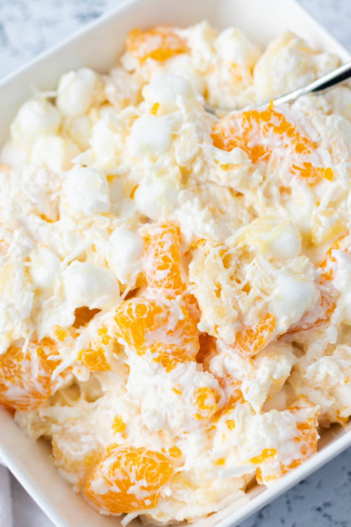 Creamy ambrosia salad in a serving bowl with pieces of Mandarin orange poking through.