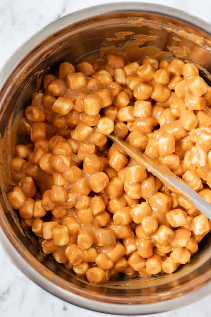 Stirring the marshmallows with the peanut butter sauce in a stainless steel mixing bowl.