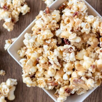 A white serving bowl filled to the brim and overflowing with caramel nut popcorn.