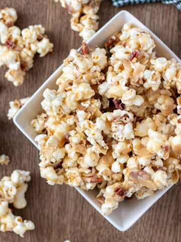 A white serving bowl filled to the brim and overflowing with caramel nut popcorn.