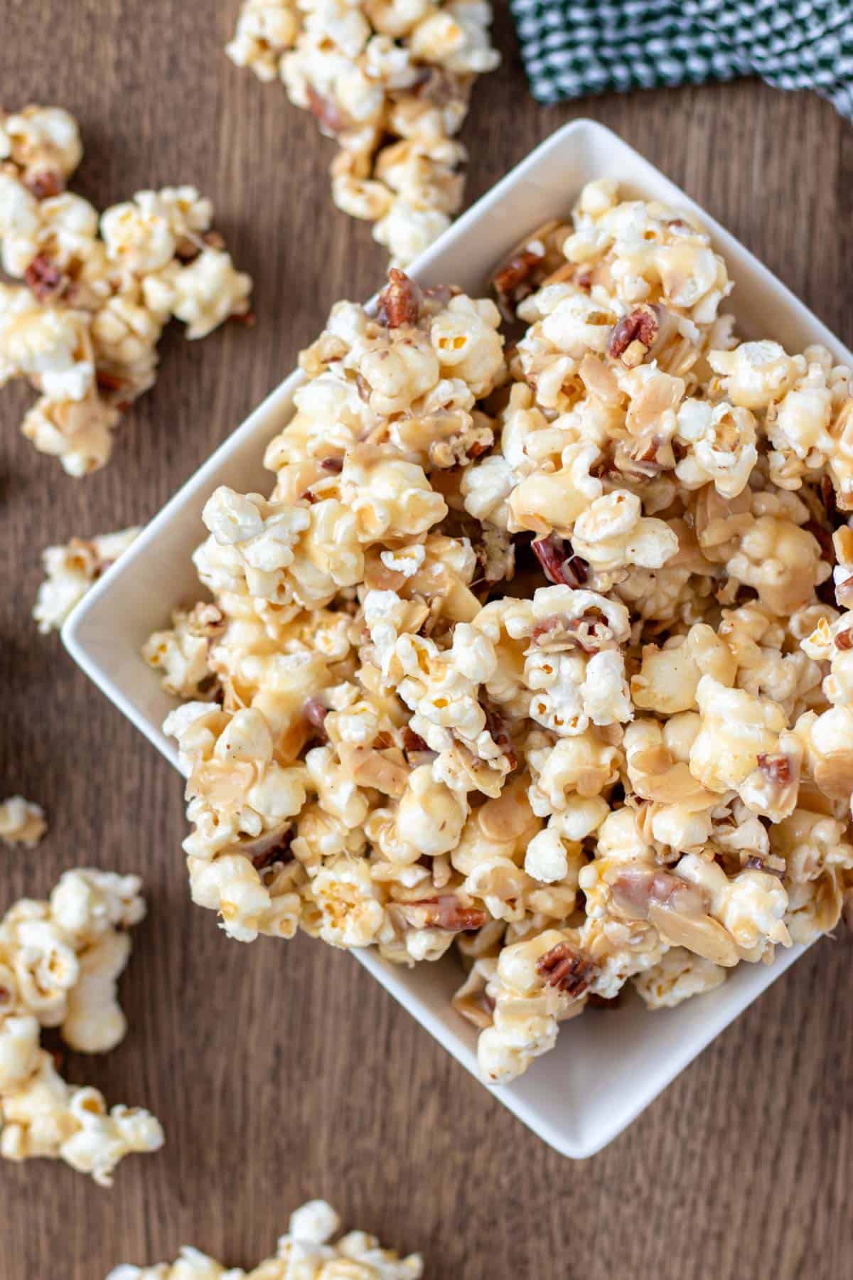 A white serving bowl filled to the brim and overflowing with caramel nut popcorn.