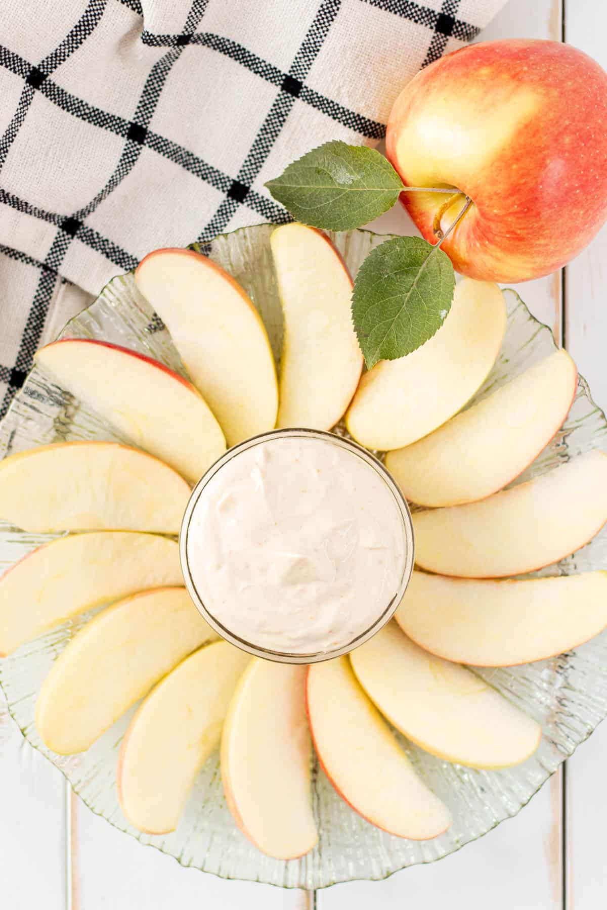 Apple dip on a plate with apple slices fanned around the jar of dip.