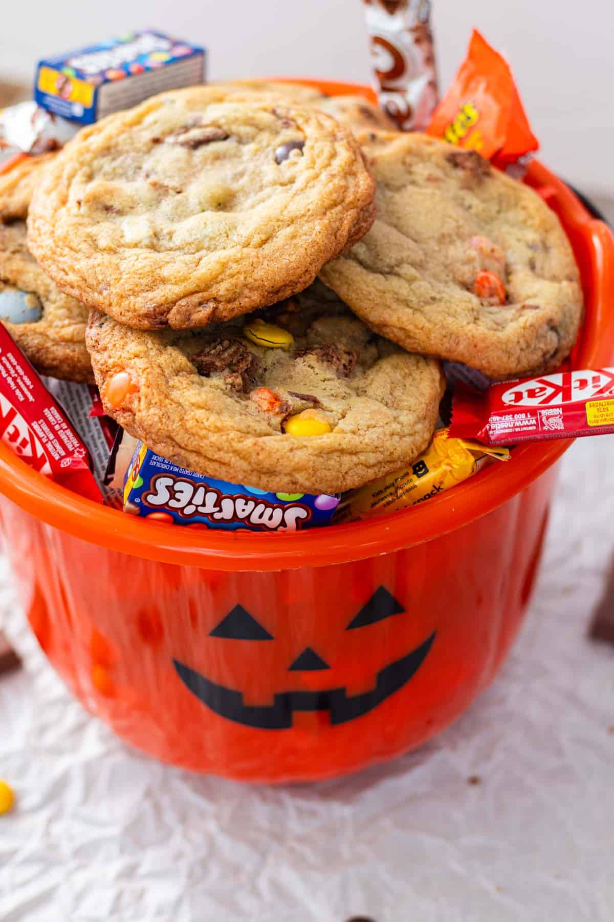 A orange pumpkin bucket filled with halloween candy and topped with prepared leftover halloween candy cookies.