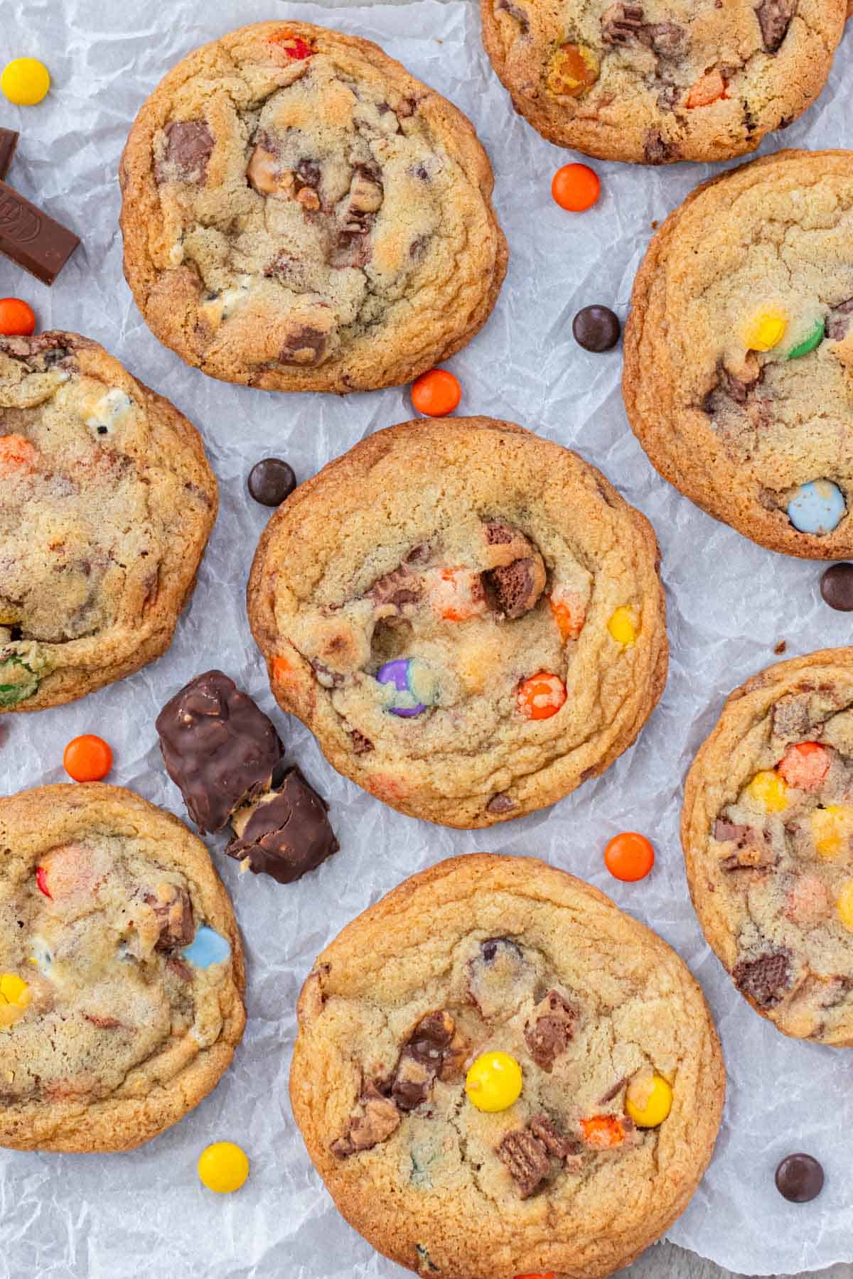 Leftover halloween candy cookies spread out on a piece of parchment paper with pieces of halloween candy sprinkled about.