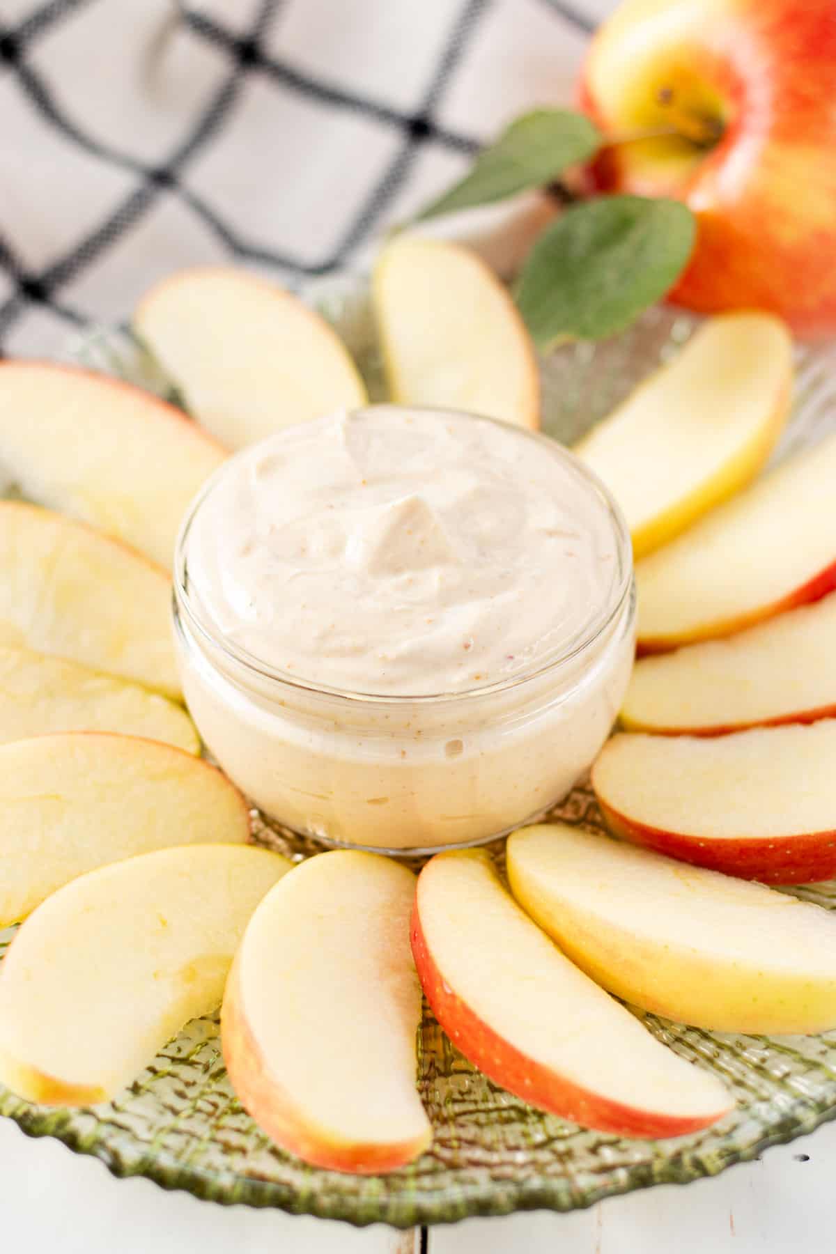 A jar of apple dip in the center of a plate with apple slices surrounding it.