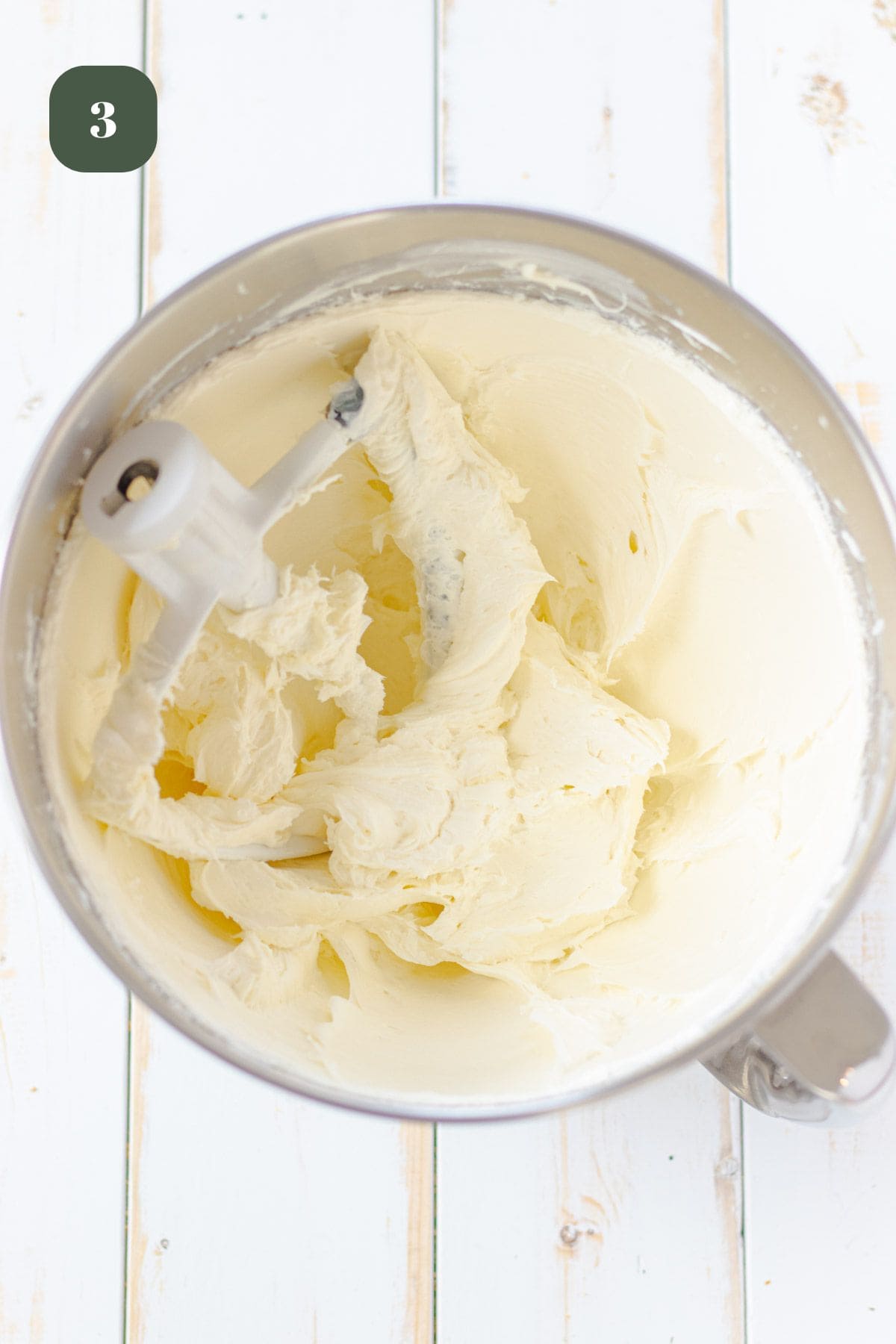 Cream cheese in a mixing bowl with a paddle mixer after it has been mixed to a fluffy consistency.