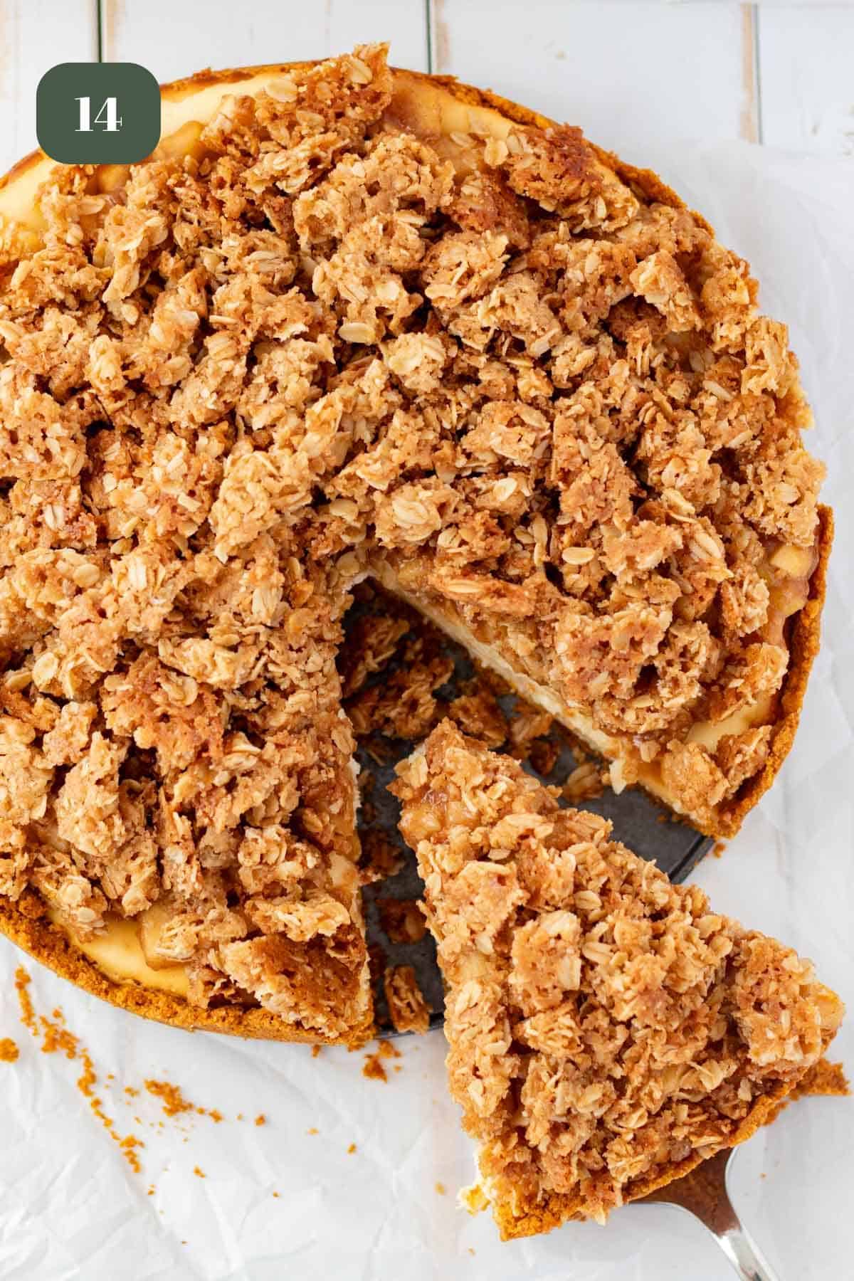 Apple crumble cheesecake with a piece being removed by a silver cake server.