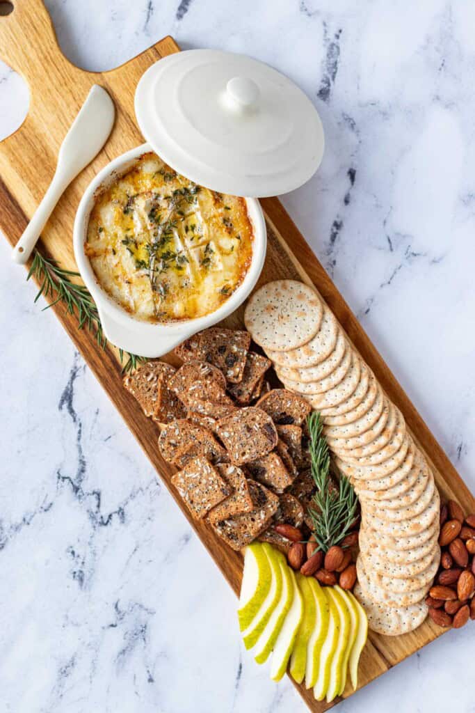 Camembert Roti on a cheeseboard with crackers, fresh pear, roasted almonds and fresh rosemary as decoration.