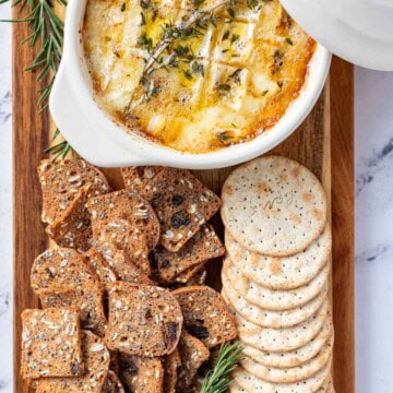 Camembert roti served on a cheese board with water crackers, multigrain fig crackers, fresh pears and roasted almonds.