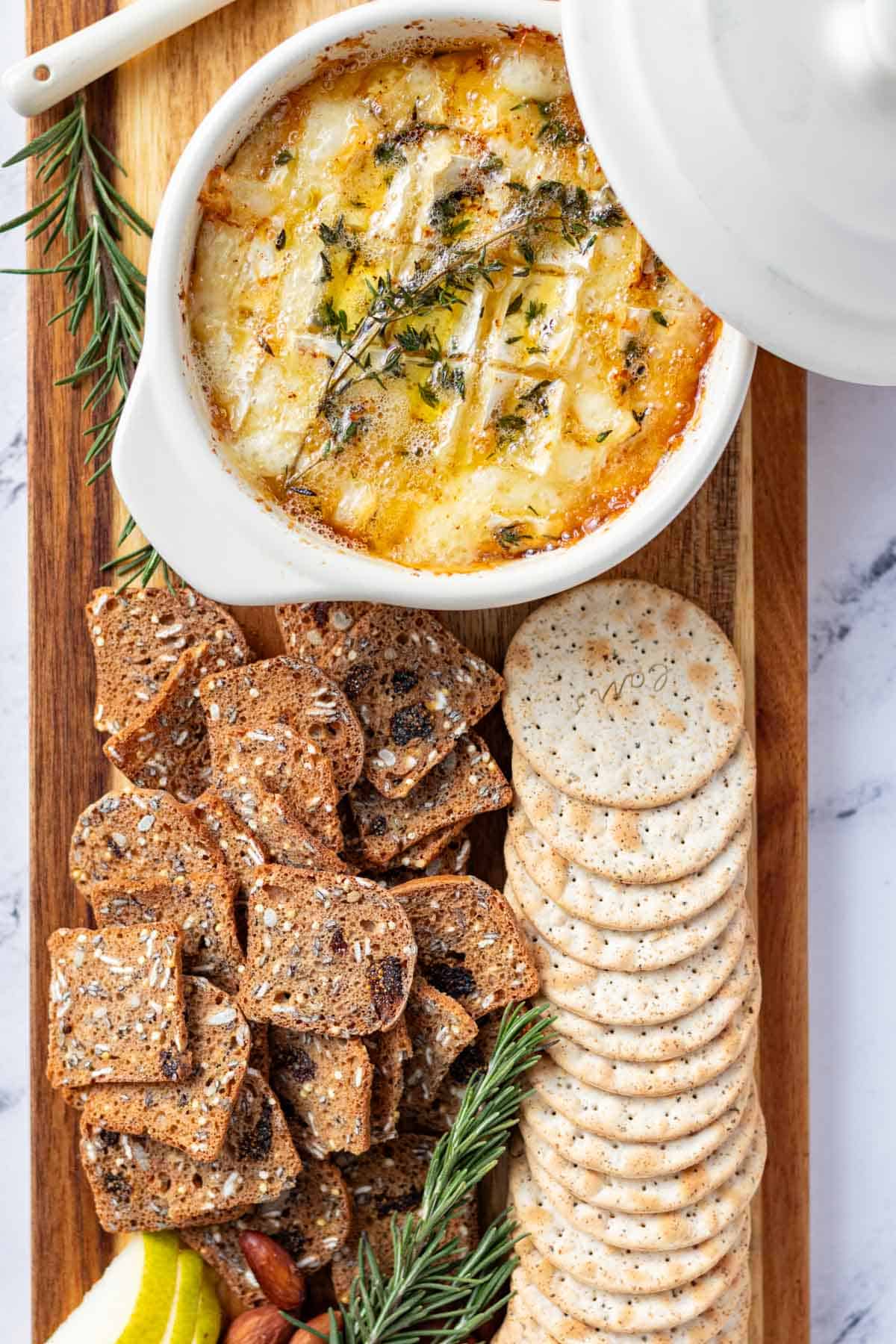Camembert roti served on a cheese board with water crackers, multigrain fig crackers, fresh pears and roasted almonds.
