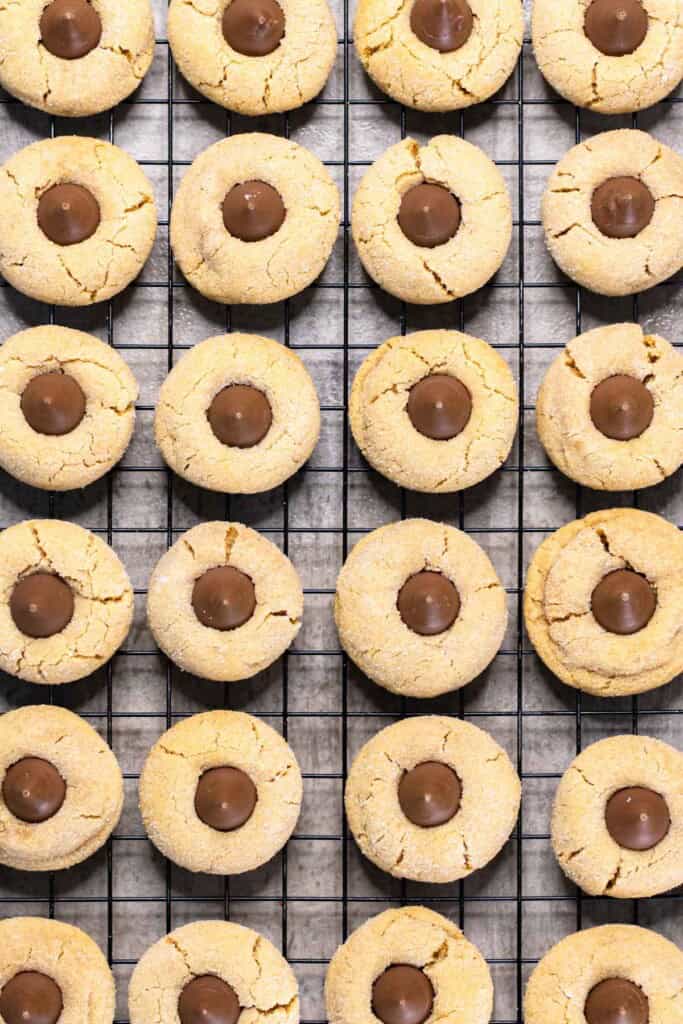 Peanut butter cookies on a cooling rack with a Hershey kiss on top of each one.