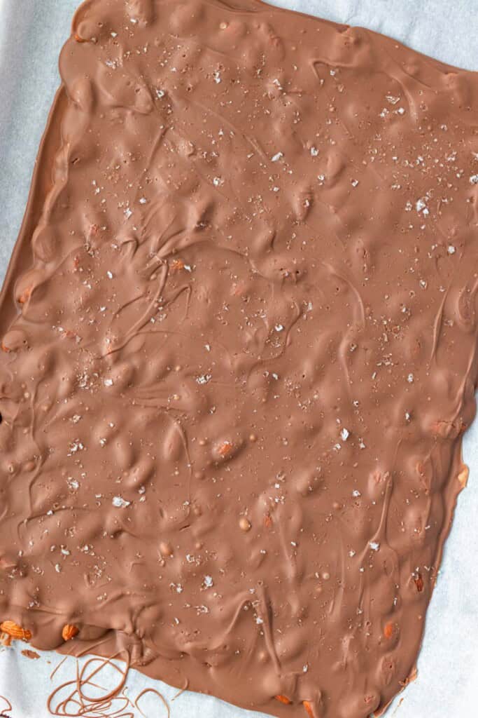 Covering the first layer of chocolate and almonds with the remaining chocolate and sprinkling with flakey salt.
