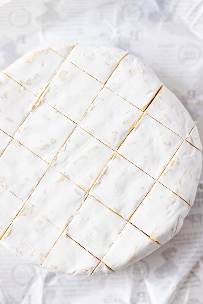 Scoring the top of the camembert cheese in a diamond pattern.