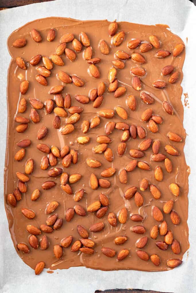 Spreading half of the melted chocolate on the parchment paper and topping with roasted almonds.