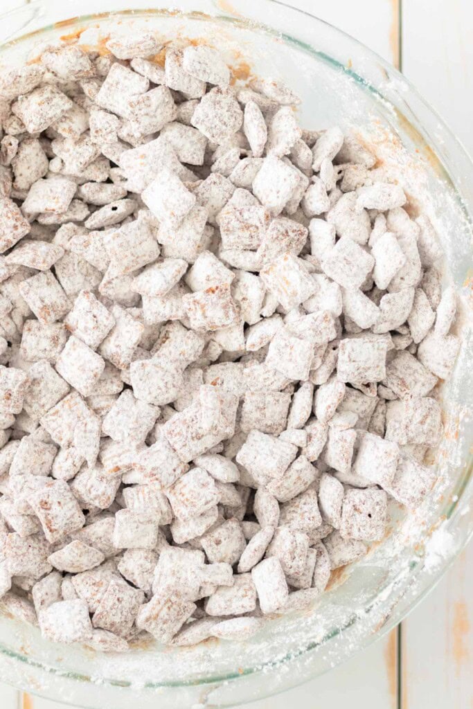 Chocolate covered Chex cereal tossed with powdered sugar in a large mixing bowl.
